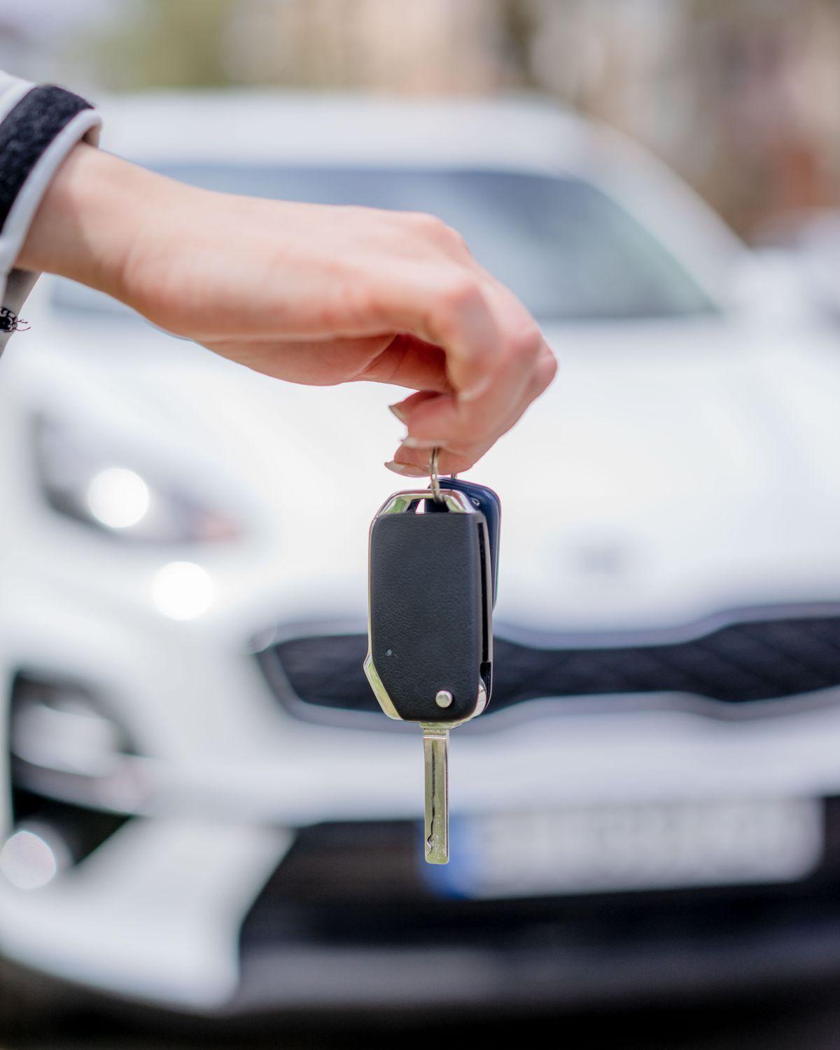 Hand hält einen Fahrzeugschlüssel, dahinter ein weißes Fahrzeug